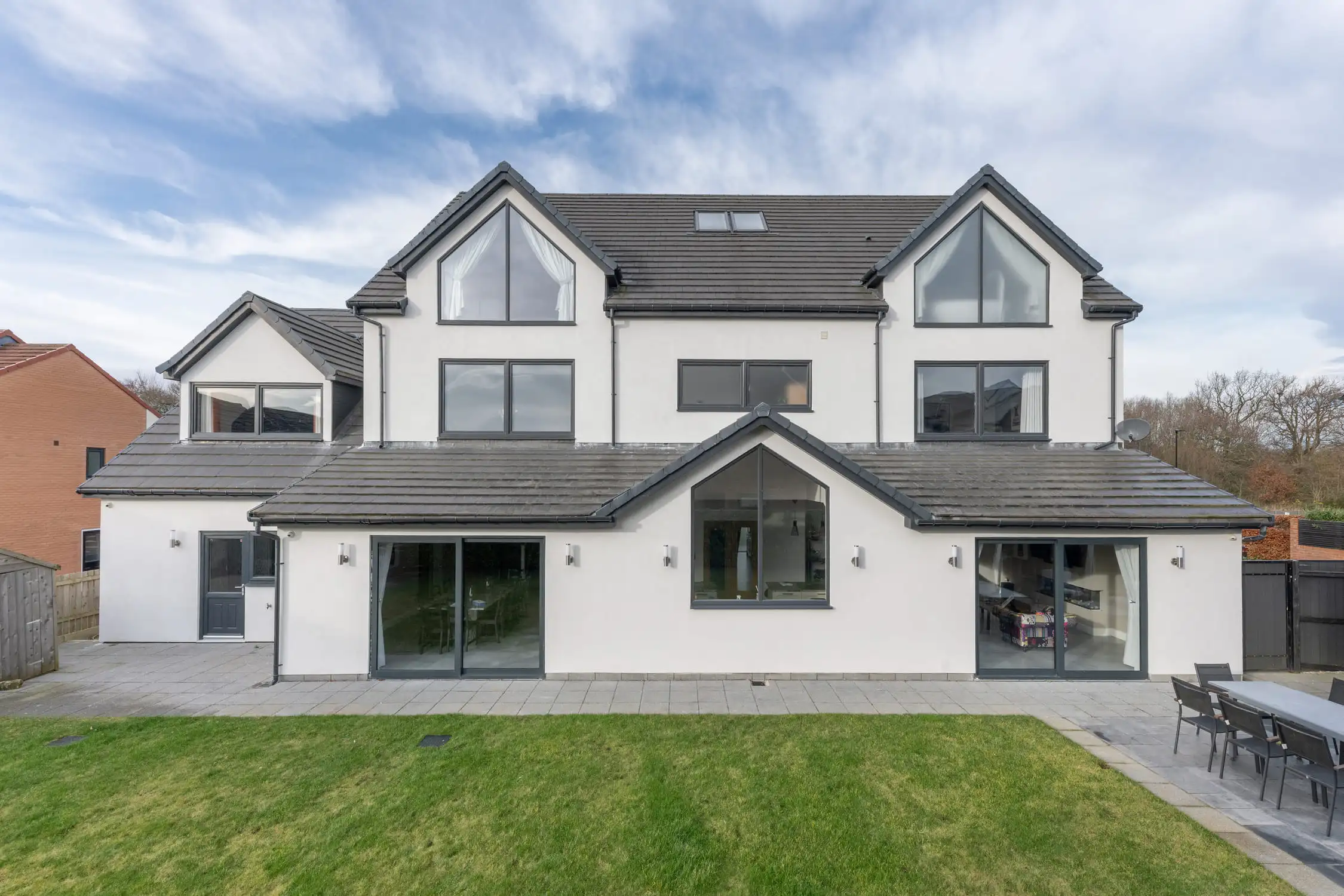 Hazelwood-Road-Great-Park-Gosforth-Newcastle-Self-Build-Home-Design-Acre-External-view-rear-white-render-pitched-roof This is the rear elevation view of the completed self-build new build project we designed on Great PArk, Newcastle. The triangular windows offer a beautiful symmetry, coupled with the pitched roofs and stunning glass elements. The grey slate roof complements the all white exterior and the anthracite window and door frames offer a modern elegance.