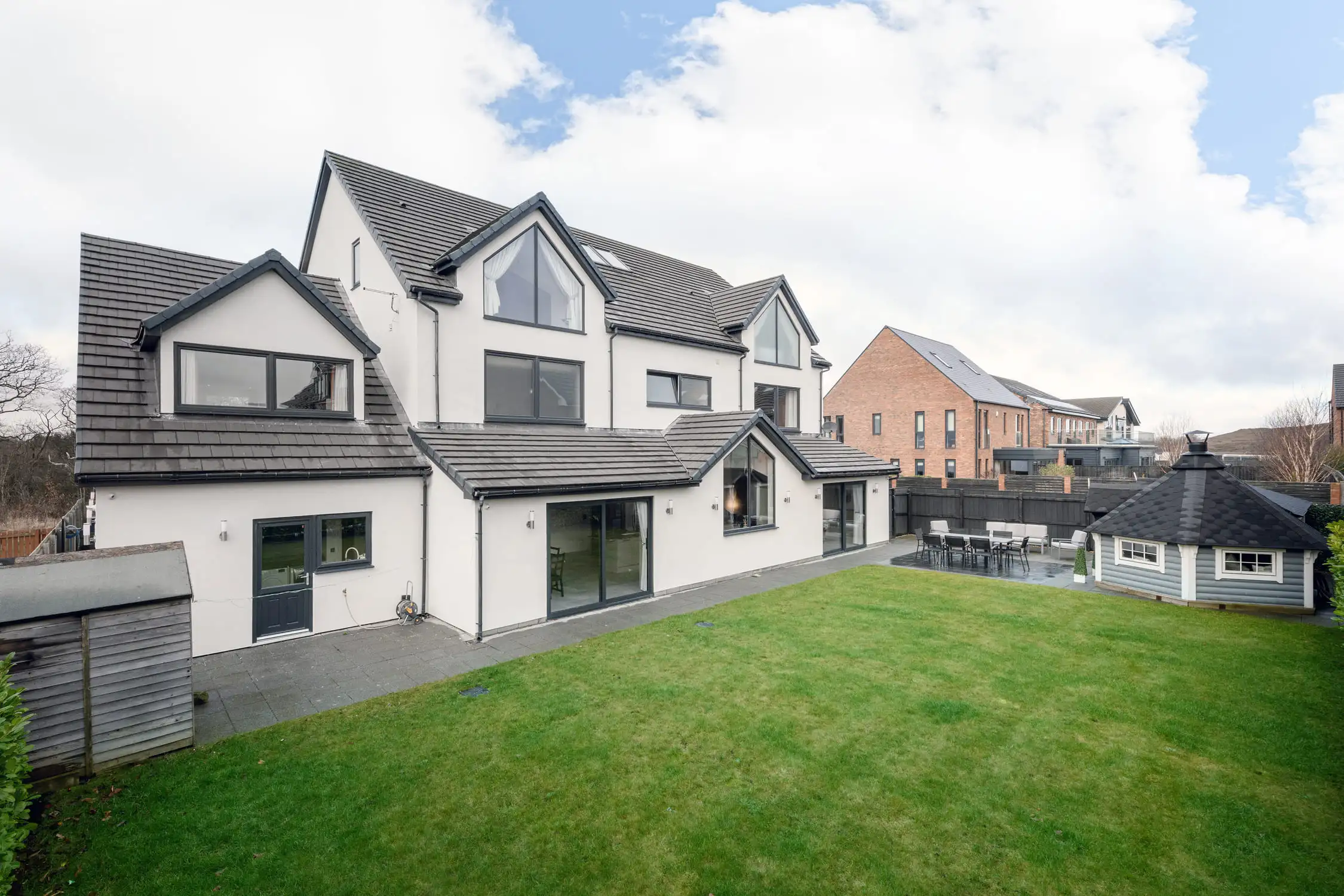 Hazelwood-Road-Great-Park-Gosforth-Newcastle-Self-Build-Home-Design-Acre-external-rear-view-daylight-garden-luxury-home-design Side angle view of the rear of a white painted self build home in Newcastle, designed by Acre Design. The slate grey roof stands proud against the blue sky and the smart, green lawn look vibrant and sharp.