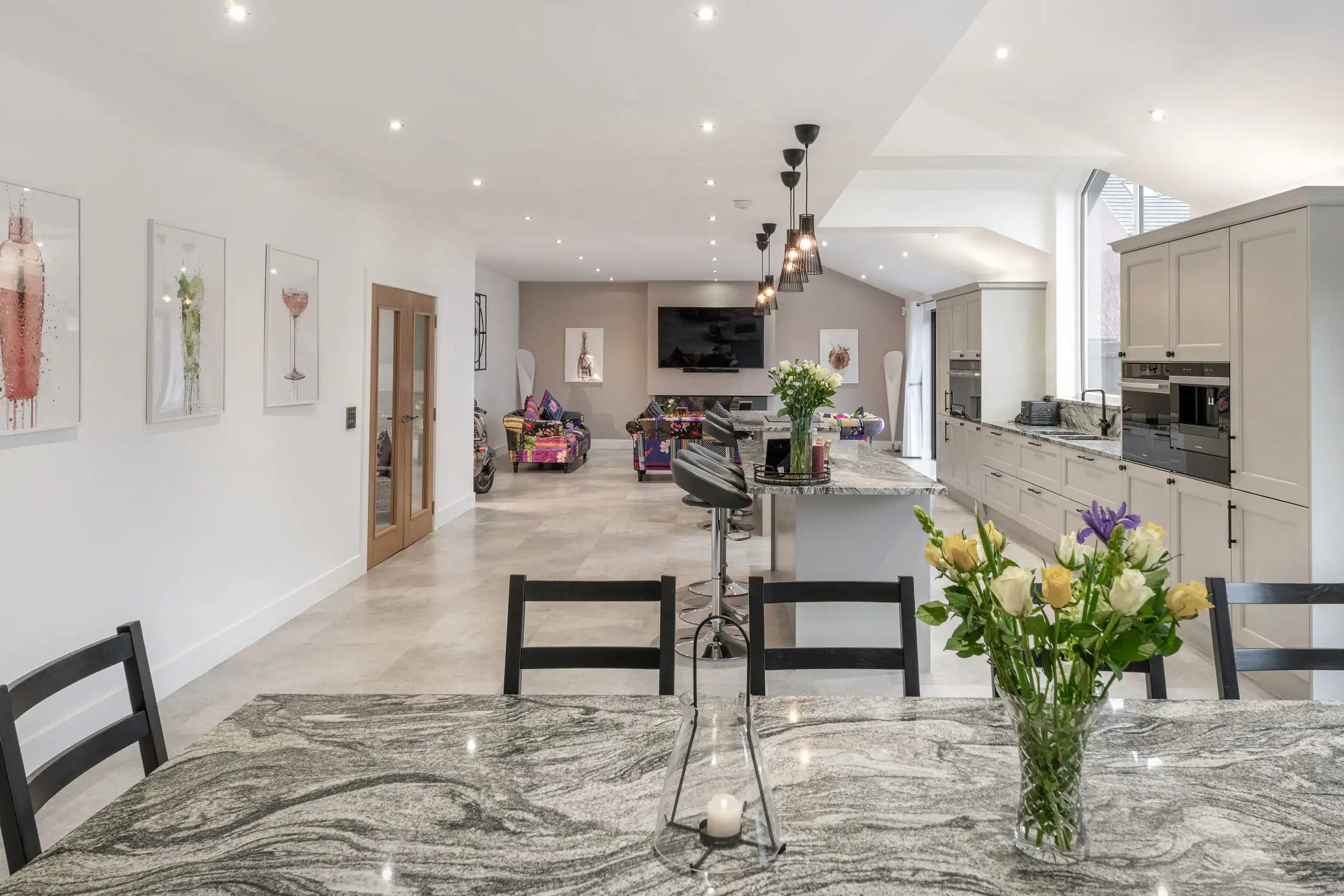 Hazelwood-Road-Great-Park-Gosforth-Newcastle-Self-Build-Home-Design-Acre-marble-kitchen-open-plan The image is framed by a marble worktop that forms and L shape around the large, open plan kitchen dining and living space. There are a bunch of spring flowers on the wroktop. The room is lit by spotlights on the minimalist white ceilings and the walls are white and fresh. There is plenty of natural light from the bifold doors and the space is calm and neutral. Large self build home designed by Acre Design Newcastle on Hazelwood Road, Great Park.