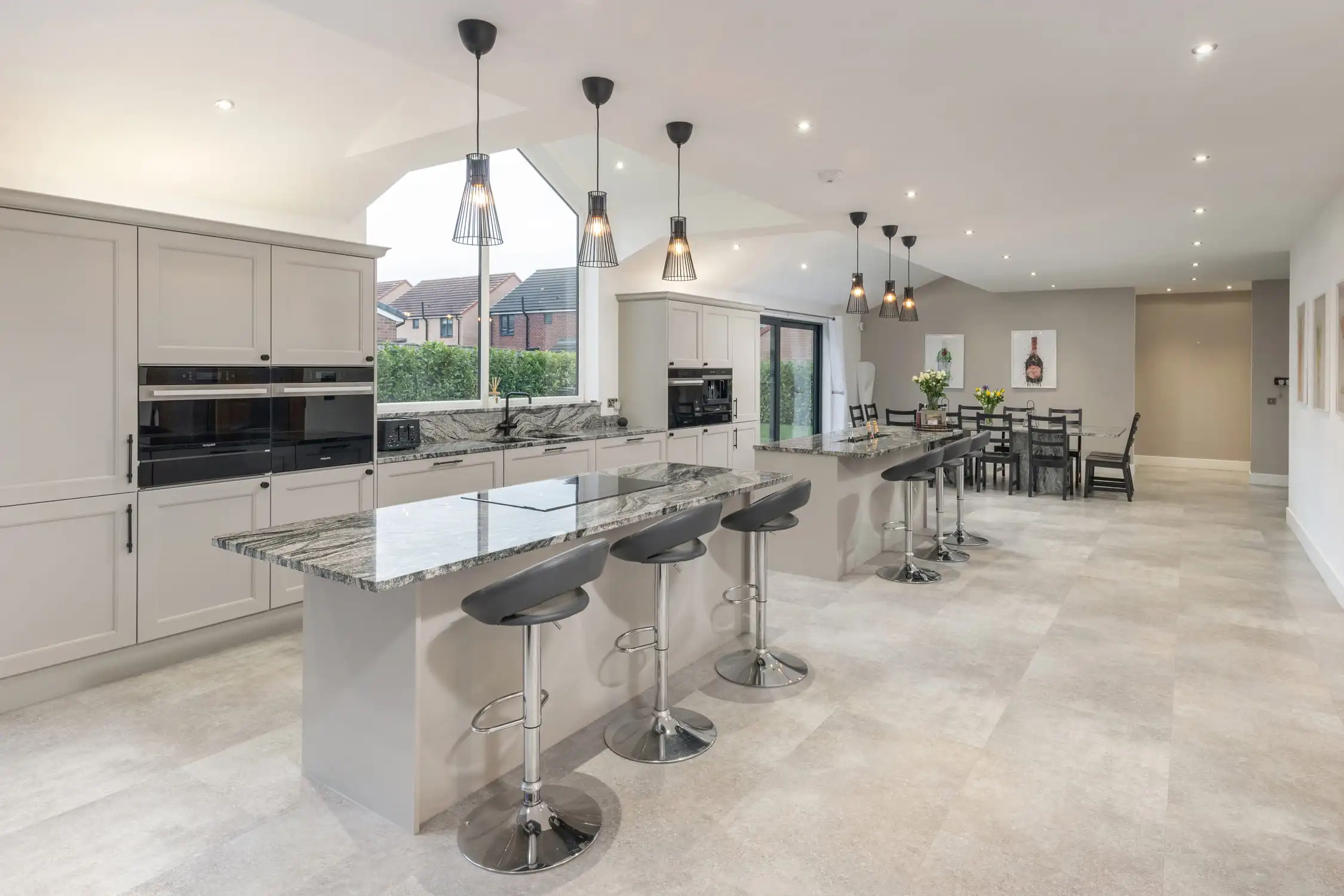 Hazelwood-Road-Great-Park-Gosforth-Newcastle-Self-Build-Home-Design-Acre-open-plan-kitchen-island-living-space Kitchen island with marble worktop and silver metal barstools with leather seats. Lit by pendant lighting and spotlights, the white room is calming and minimalist. Modern marble floor tiles keep the space light and fresh and the large windows incorporate plenty of natural light. Large self build home designed by Acre Design Newcastle on Hazelwood Road, Great Park.