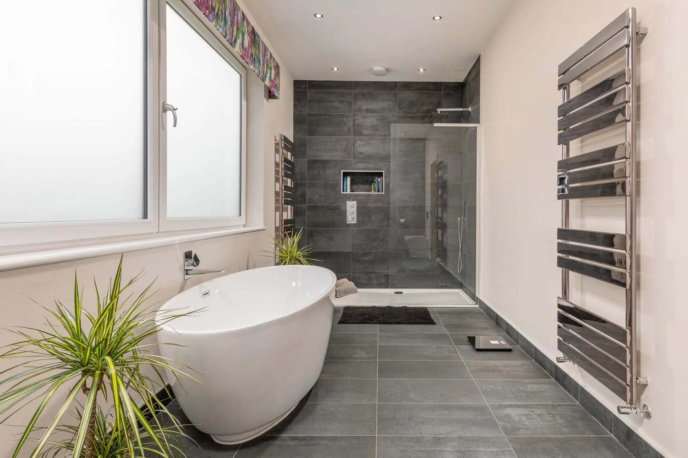 Hazelwood-Road-Great-Park-Gosforth-Newcastle-Self-Build-Home-Design-Acre-sleek-bath-oval-egg-shaped-tiles-slate Large self build home designed by Acre Design Newcastle on Hazelwood Road, Great Park. Oval shaped white bath in a large family bathroom, tiles in grey with an extra large open shower enclosure and rainforest shower fittings.